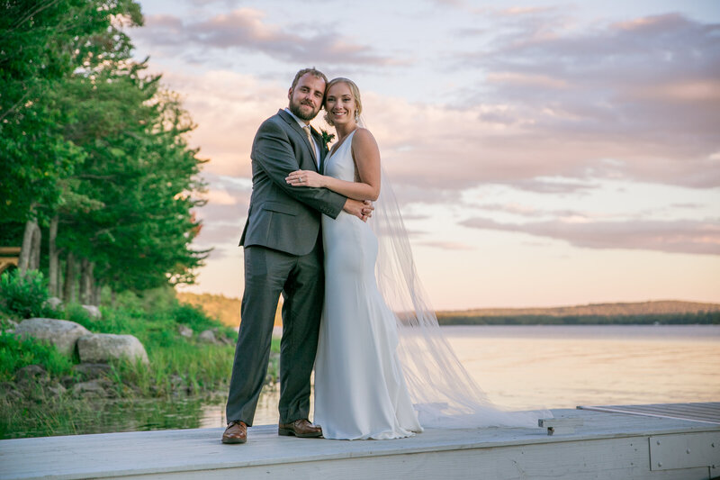 Bride and Groom holding each other standing on dock at sunset | Wedding Photography at Klein Wedding at Grace on the Lake