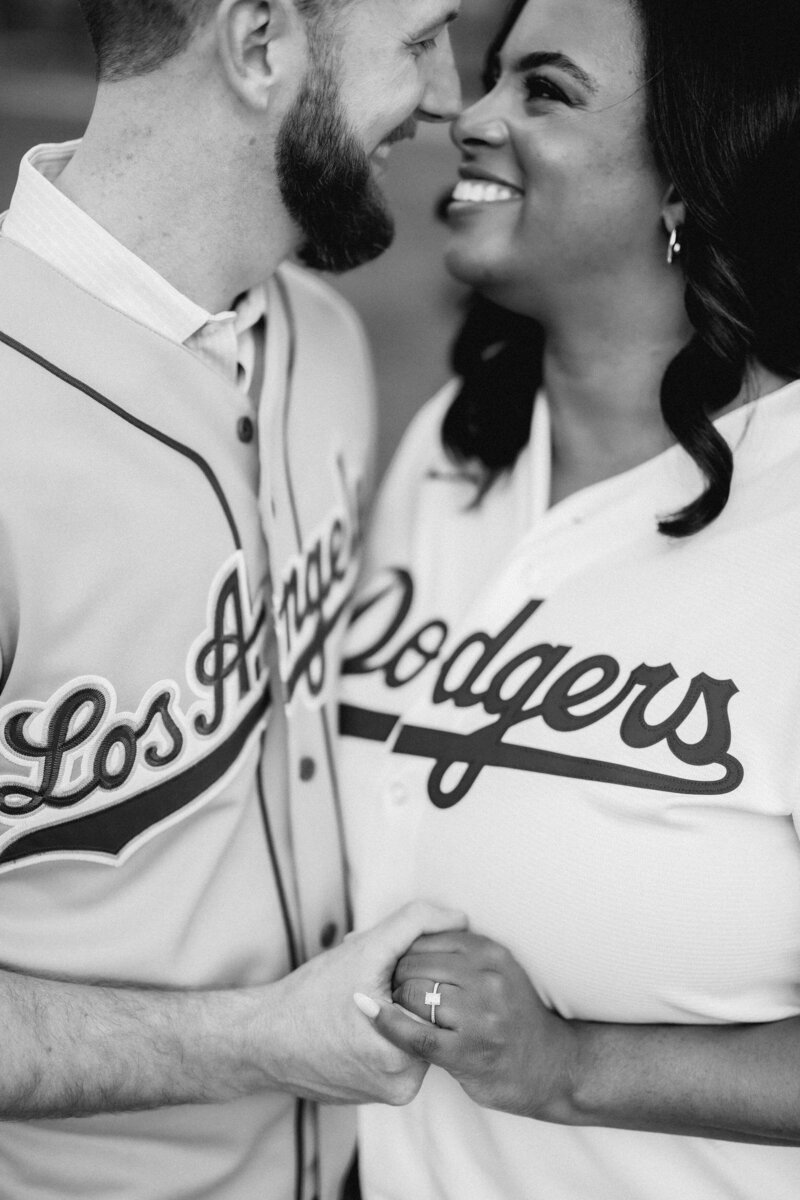 A couple standing close and smiling as they hold hands showing off an engagement ring 