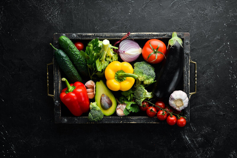 fruit and vegetables in a dark wood box on a slate background
