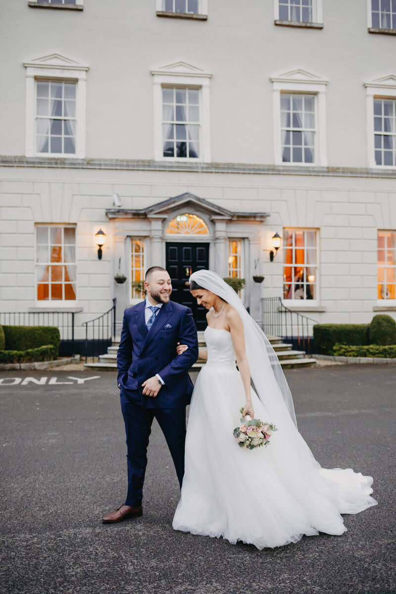 Newlyweds sharing a happy walk in front of their venue, Dunboyne Castle, dressed in classic wedding attire