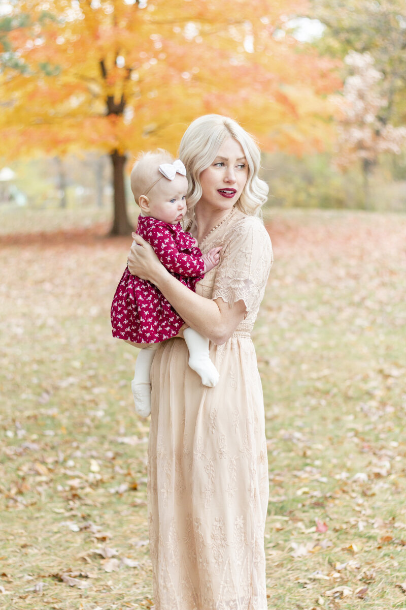 a mother holding her baby with orange fall leaves in the backgroud
