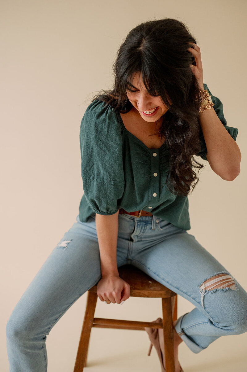 Woman sitting on a stool looks down and plays with her hair