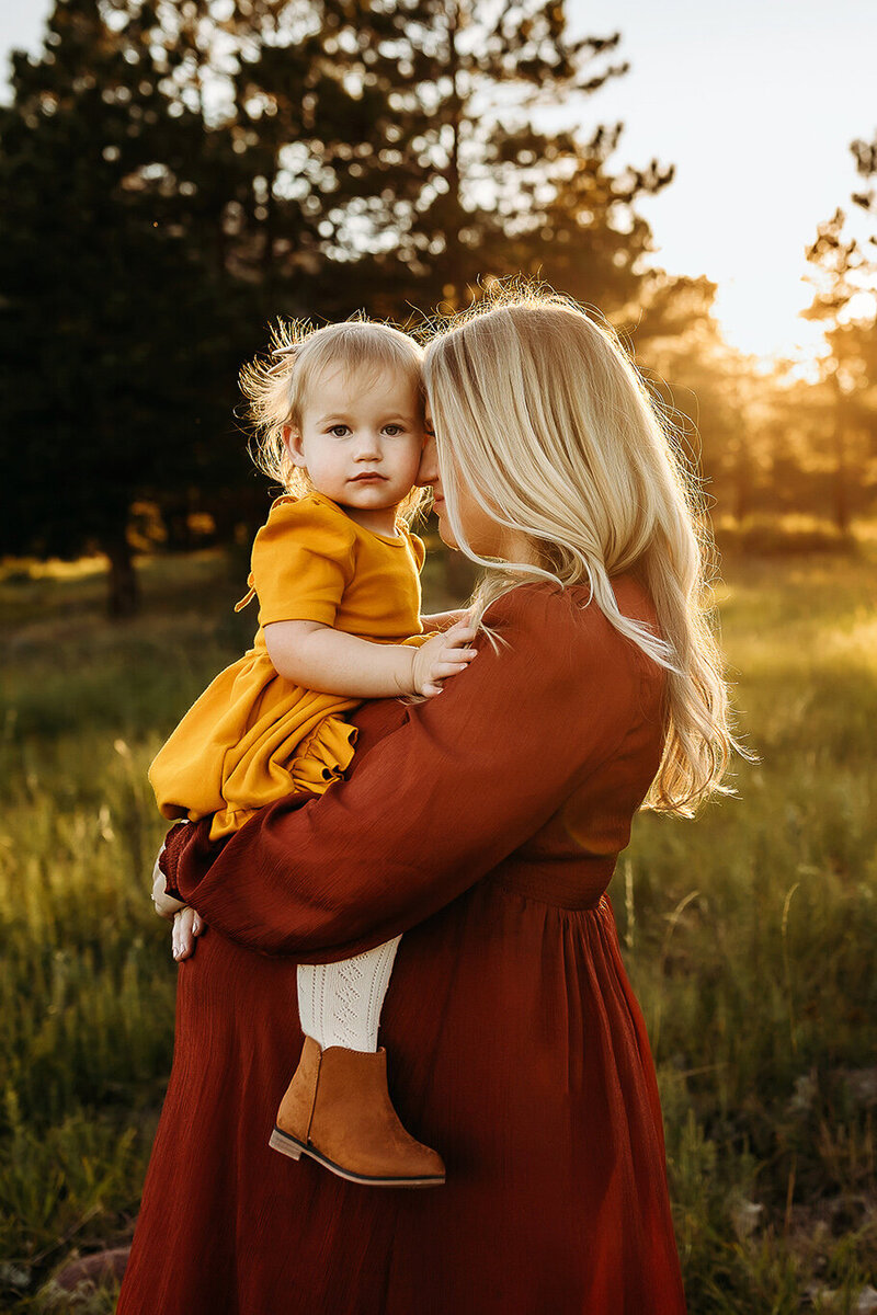 Expecting mom in a flowy red dress snuggling her toddler daughter at sunset in the Boulder mountains.