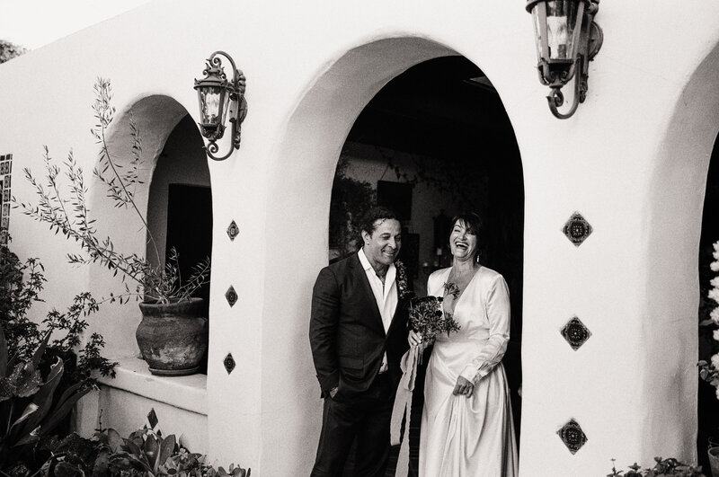 Black and white film photo of a joyful couple standing in an arched entryway during their micro wedding in San Diego — a candid and heartfelt moment by a film wedding photographer.