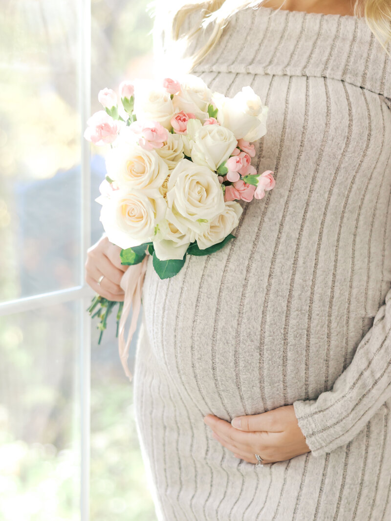 Maternity photography in minneapolis studio - showing a woman holding her belly and a bouquet of flowers.  Taken by Angela Watts Photography.