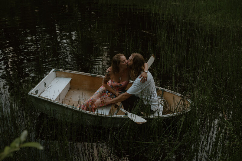 A newlywed couple kisses while sitting in a canoe on a pond.