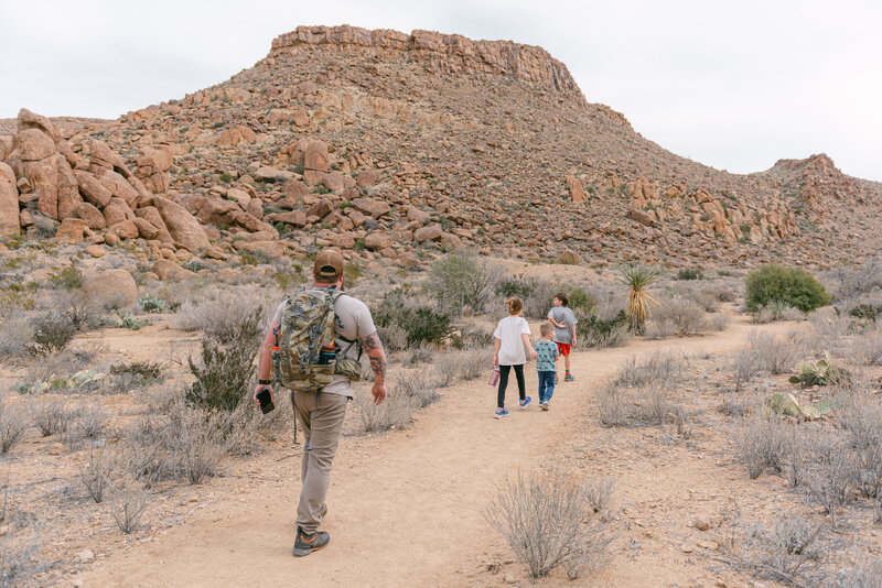Color photograph of a father and three children standing at the edge of a canyon in Big Bend, Texas. Editorial, luxury family imagery captured by Erin Marcin Photography, highlighting natural textures, high-end storytelling, and organic light in a dramatic desert landscape.