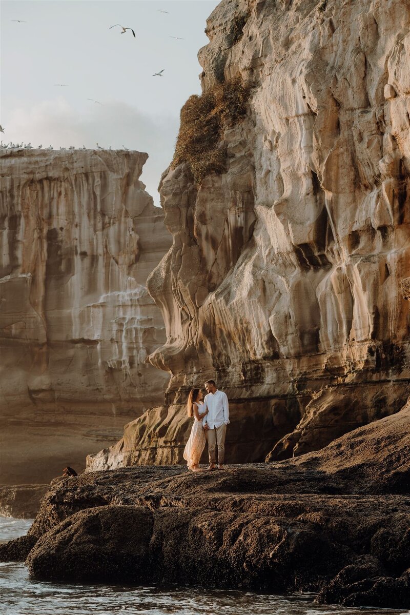 A couple standing on the rocks below the gannet colony in Muriwai Auckland while being photographed by Waikato Photographer Haley Adele Photography