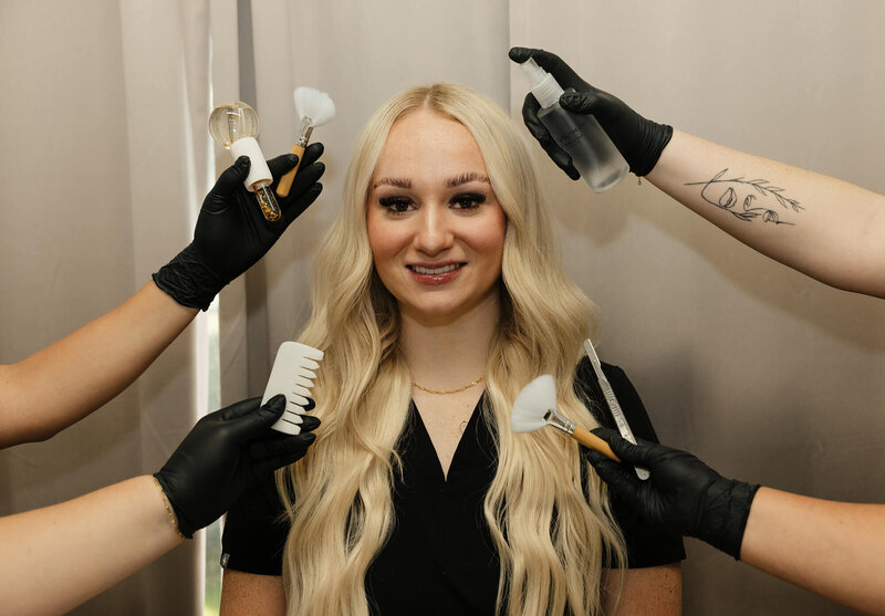 A nurse surrounded by hands holding different aesthetic and beauty tools such as a spray bottle, brushes for facials, and a comb.