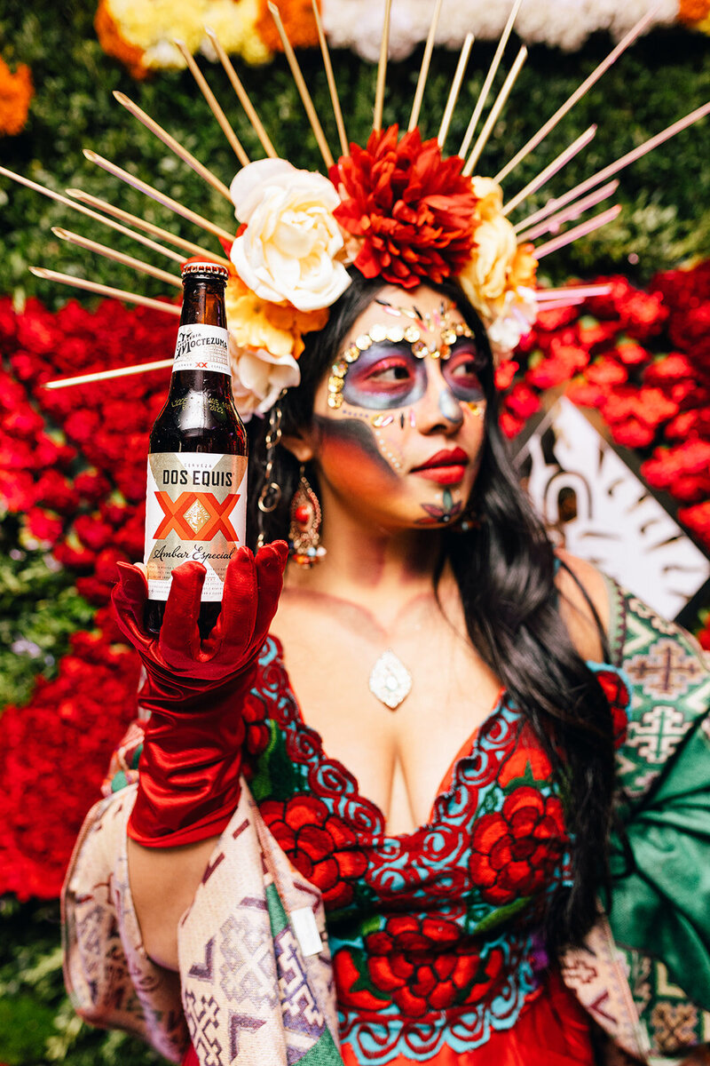 lady holding a bottle of Dos Equis dressed in red for Dia De Los Muertos
