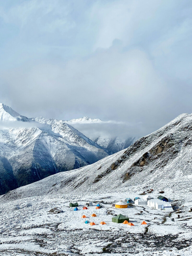 Snow-covered Himalayan landscape with colorful tents at a high-altitude base camp beneath dramatic peaks.