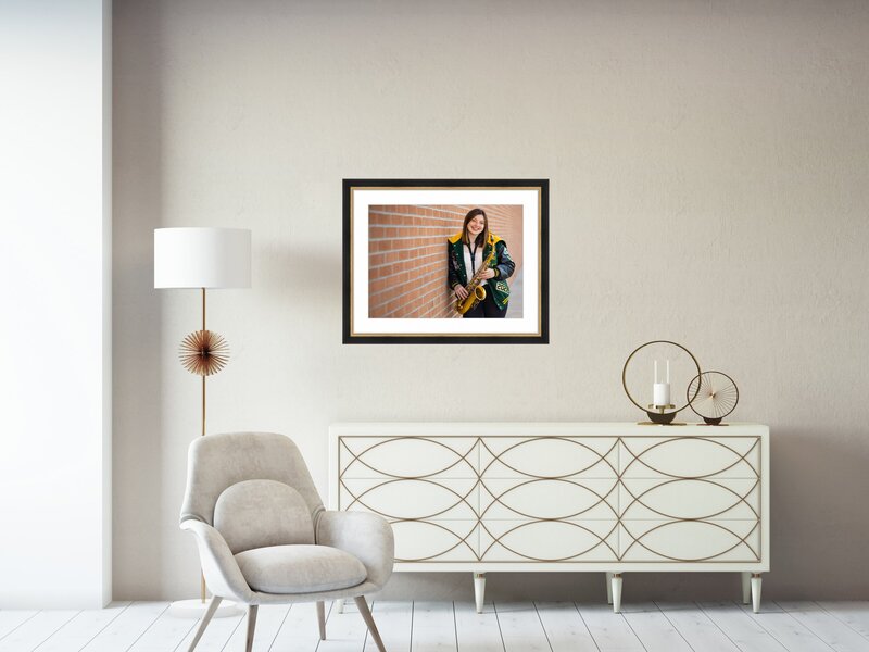 framed portrait of a high school senior hanging on a wall above a chair and side table