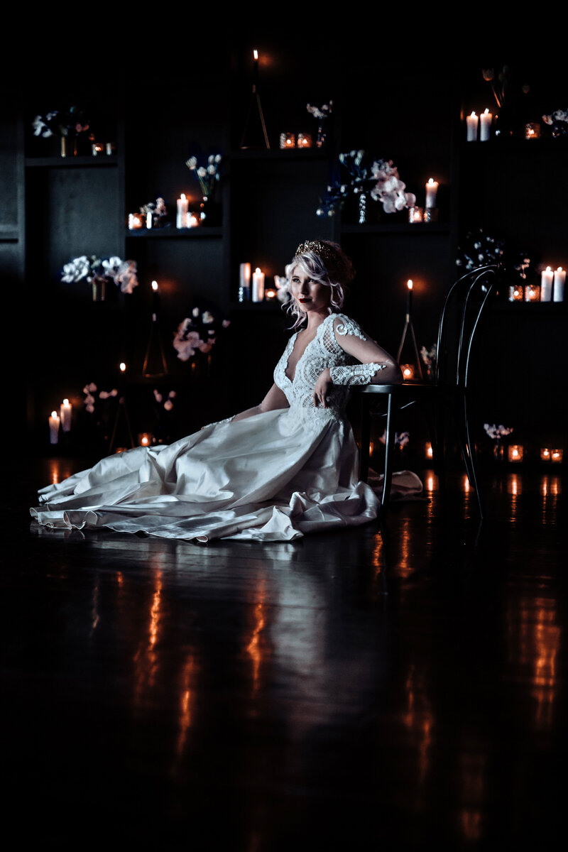 Bride sitting on floor of dark moody candlelit wedding reception in lace wedding dress