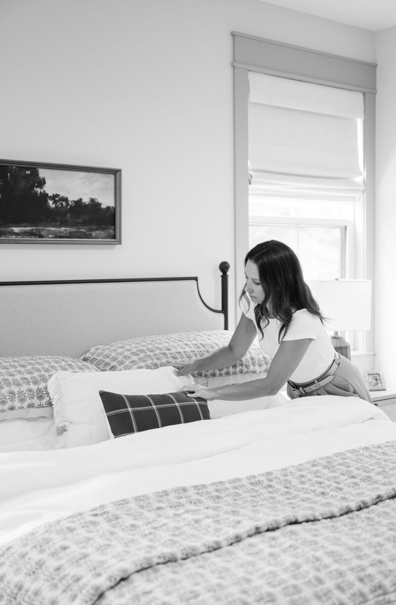 Abby Lucas fluffing a brown pillow in a white bedroom