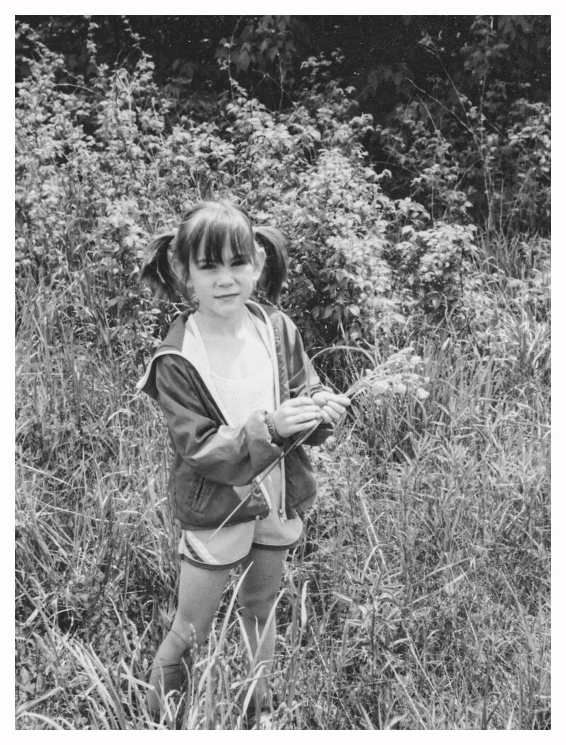 A young girl with pigtails picking flowers in a field. 