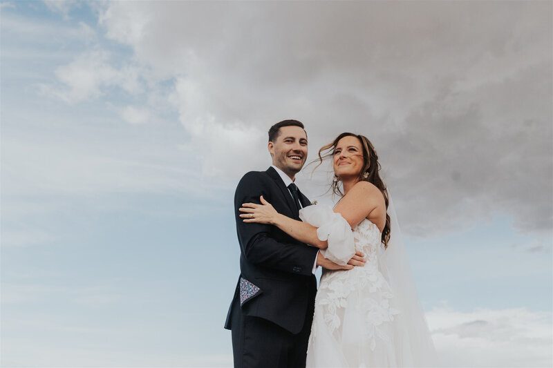 A bride and groom smile with the clouds in the background on their wedding day 