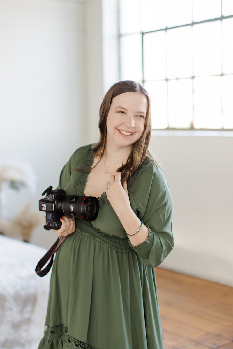 Photographer holds camera and looks off camera and smiles while twirling hair