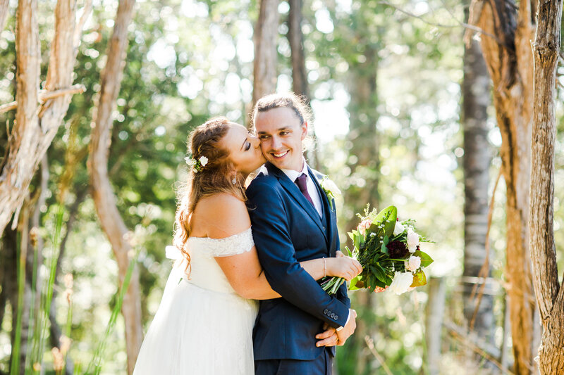 bride and groom snuggling in forest on sunny day