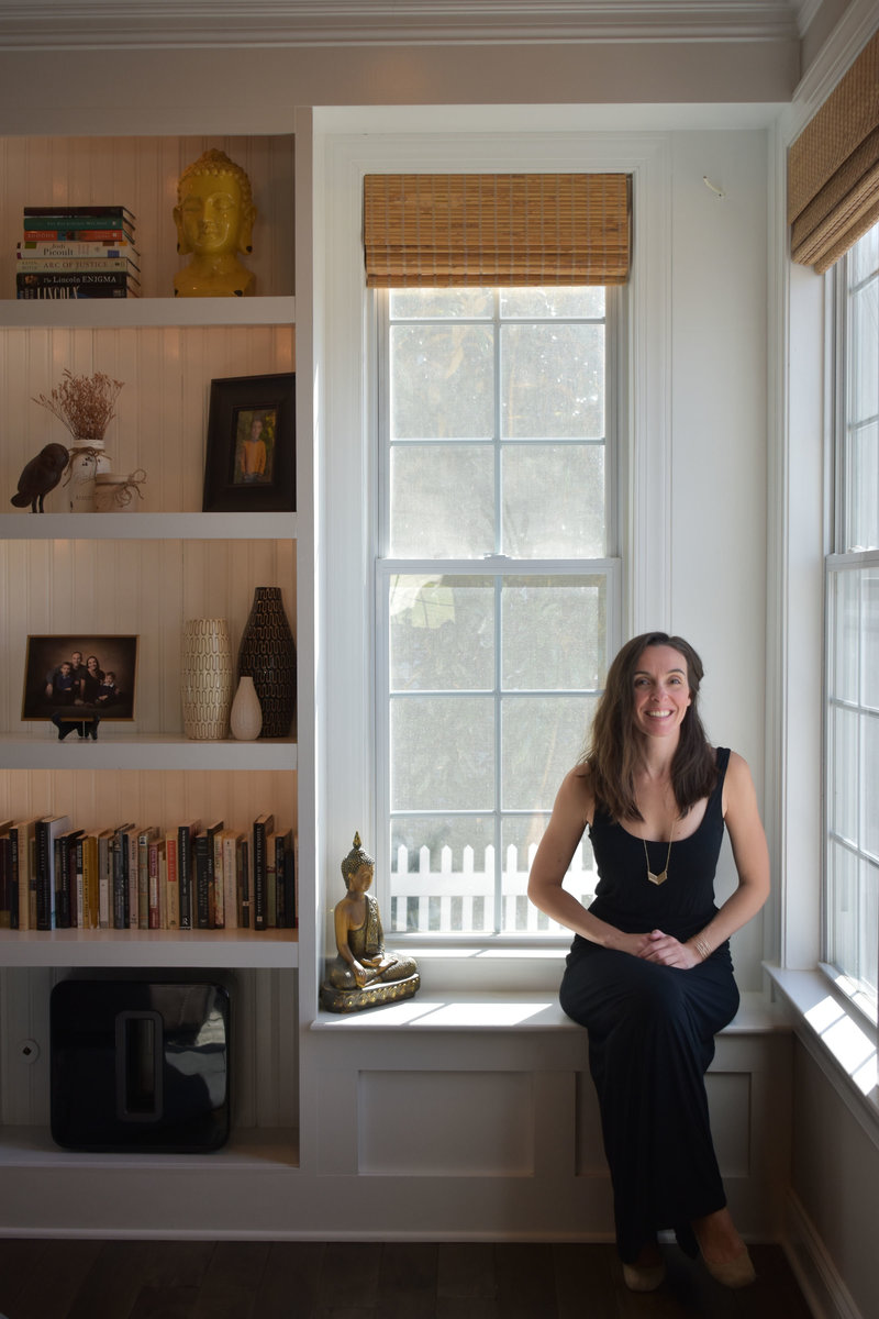 Christine Camarda seated in front of window with buddha, books, vases, photographs and other decor items as inspiration