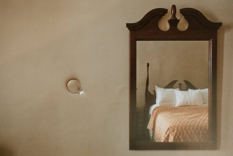 A creative shot of an engagement ring floating beside a mirror that reflects a neatly made bed, symbolizing love and anticipation.