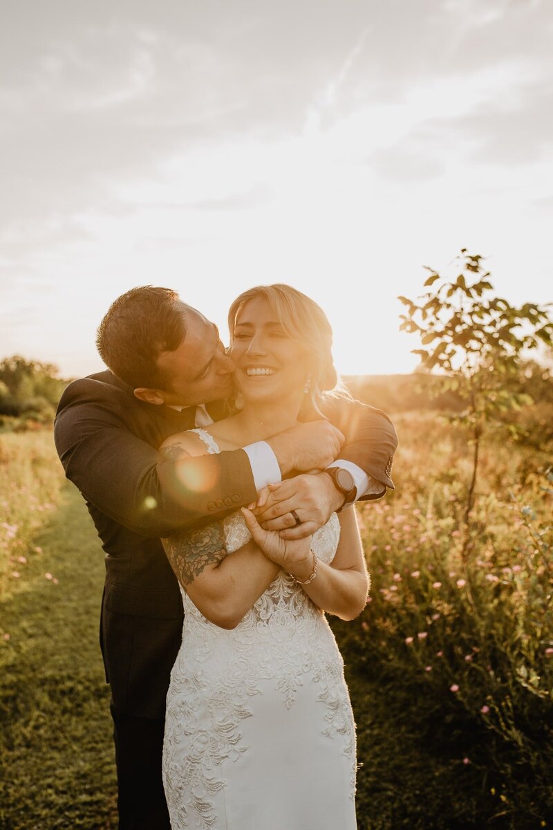 Man and woman on their wedding day hugging with warm golden sun behind them