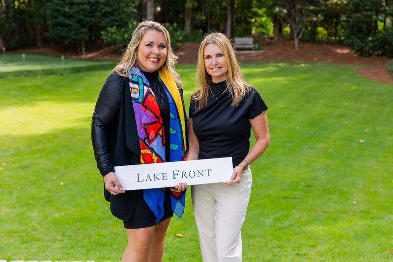 realtor women team holding a Lake Front sign in a house back yard during photoshoot