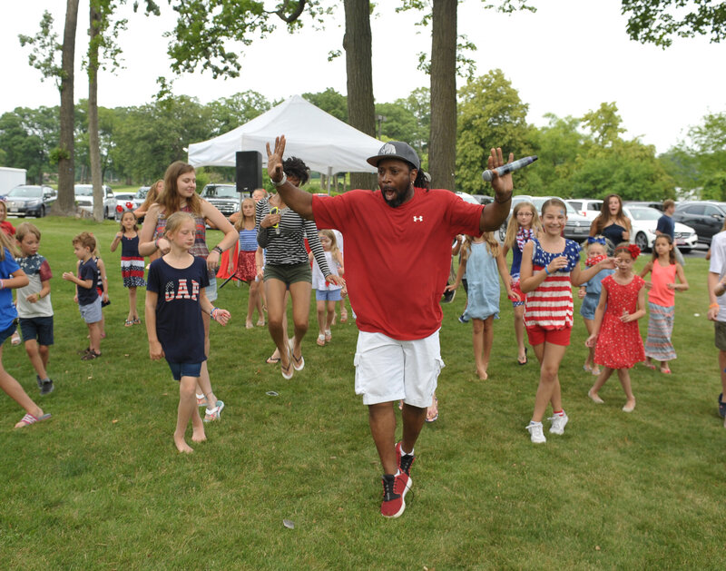 DJ mid-jump leading a dance with kids outside