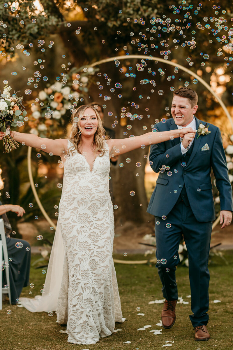 Newlywed couple running down the aisle through a cloud of glittery bubbles