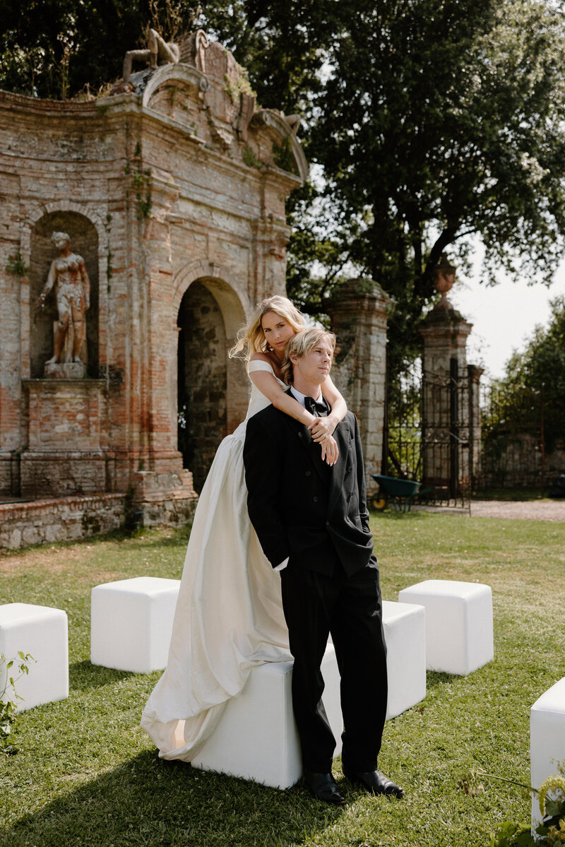 A person standing behind their partner with their arms over their shoulders on their wedding day 