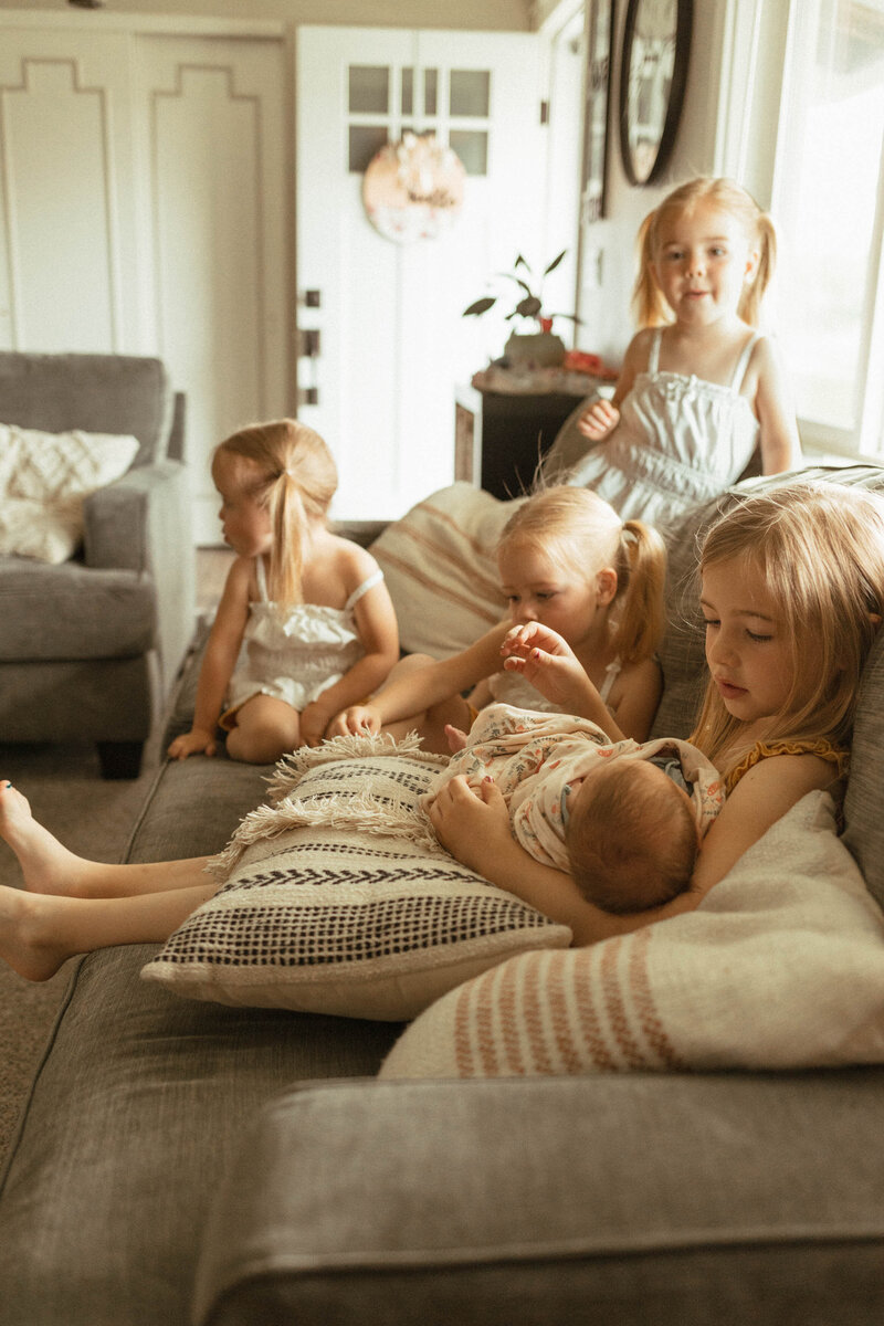 Four young sisters holding their new baby brother on the sofa.