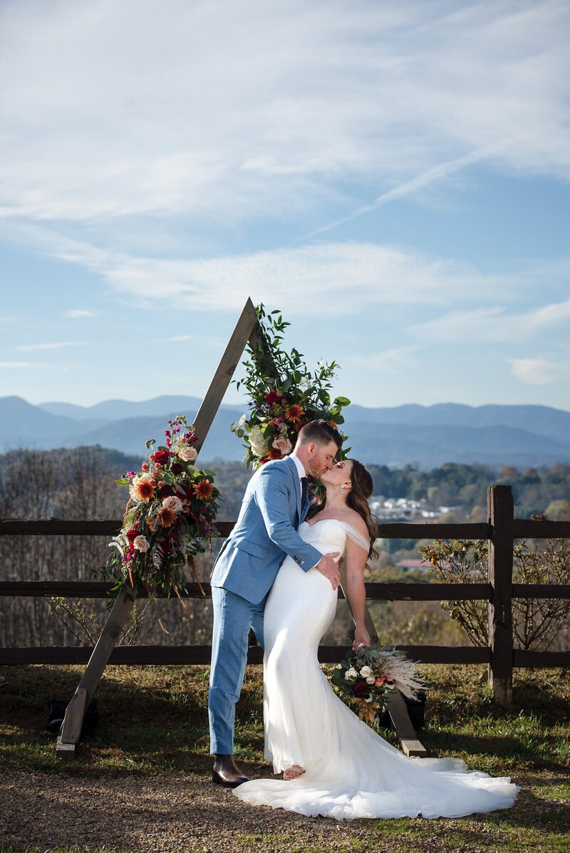 Groom dipping bride in front of arbor outside in Asheville with the Blue Ridge mountains in the background by Charlotte wedding photographers DeLong Photography