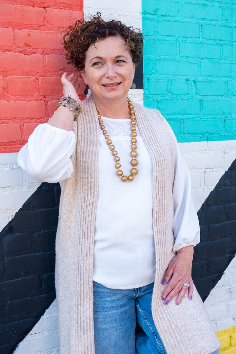 Tammy Aston smiling in front of a colorful brick wall, introducing herself as a wellness coach, military veteran, and survivor.