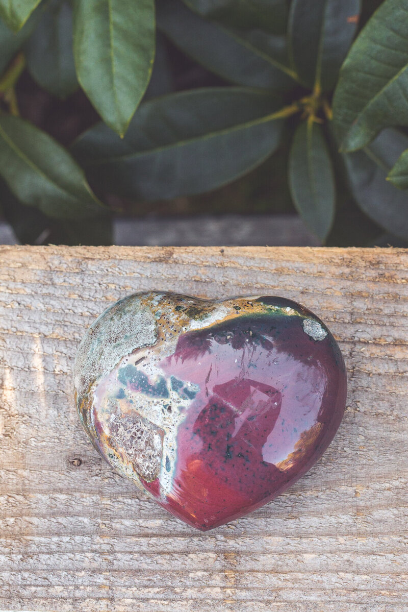 The back side of a moss agate heart crystal with green and burgundy colours.