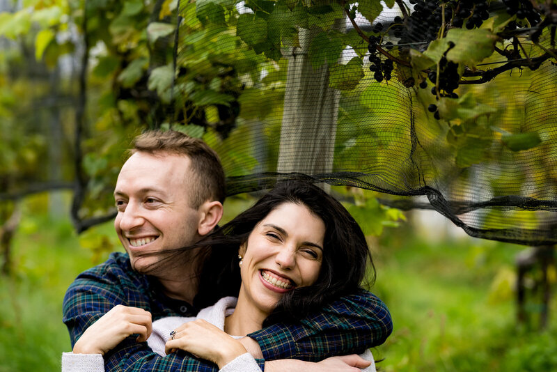 Couple sitting close and snuggling in a vineyard, holding hands and laughing together at Taylor Brooke Winery, Woodstock CT