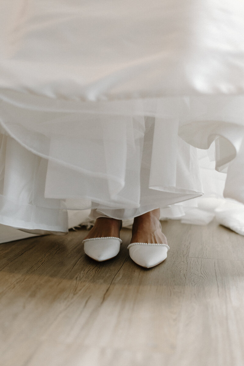A PAIR OF WHITE SHOES PEEKING OUT FROM A WEDDING DRESS
