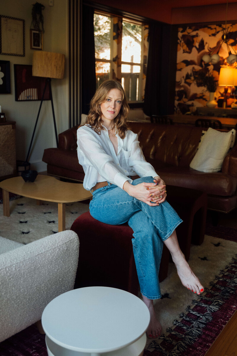Interior Designer Erin Lima sits on a stool in her home, which showcases bold and eclectic home decor.