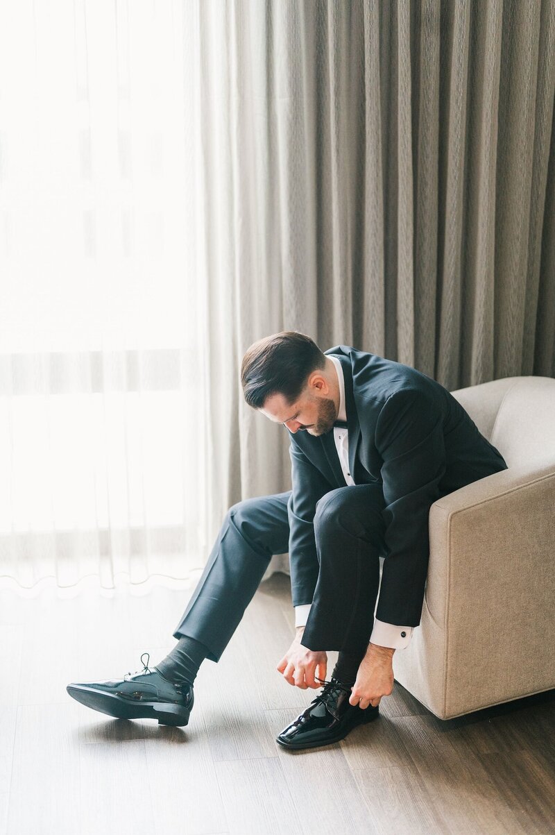 A groom leans over and ties his shoe lace.