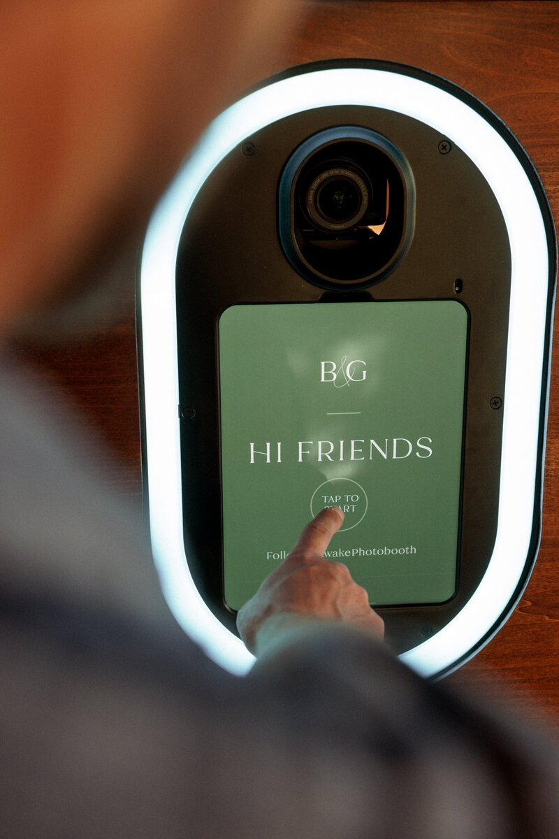 Hand reaching out to touch start on the photo booth start screen that reads 'hi friends'