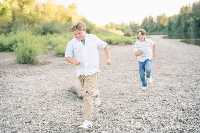 boys run along the river at a candid family photo session near portland, oregon