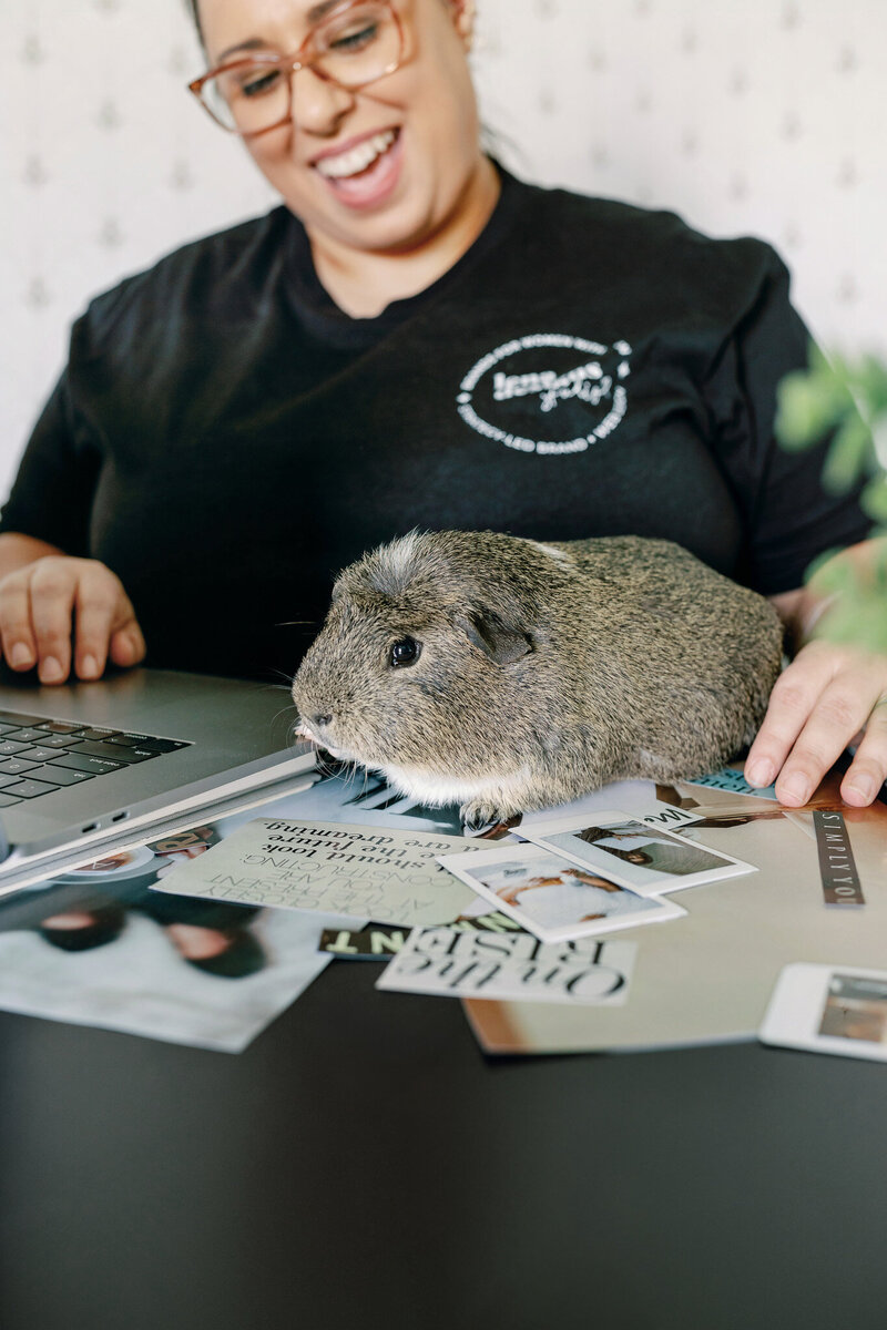 Lena working in her office with her grey and white guinea pig on the desk with her.