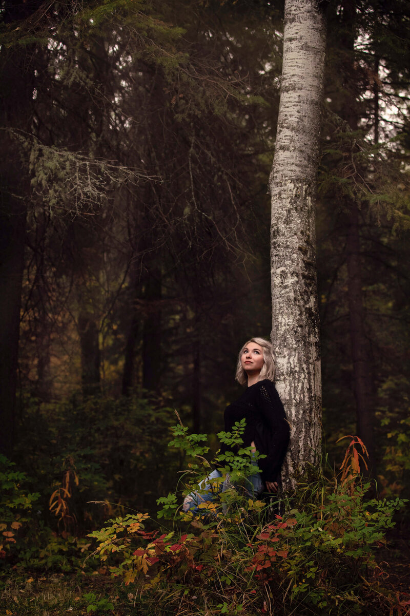 blonde girl leans on tree in the forest