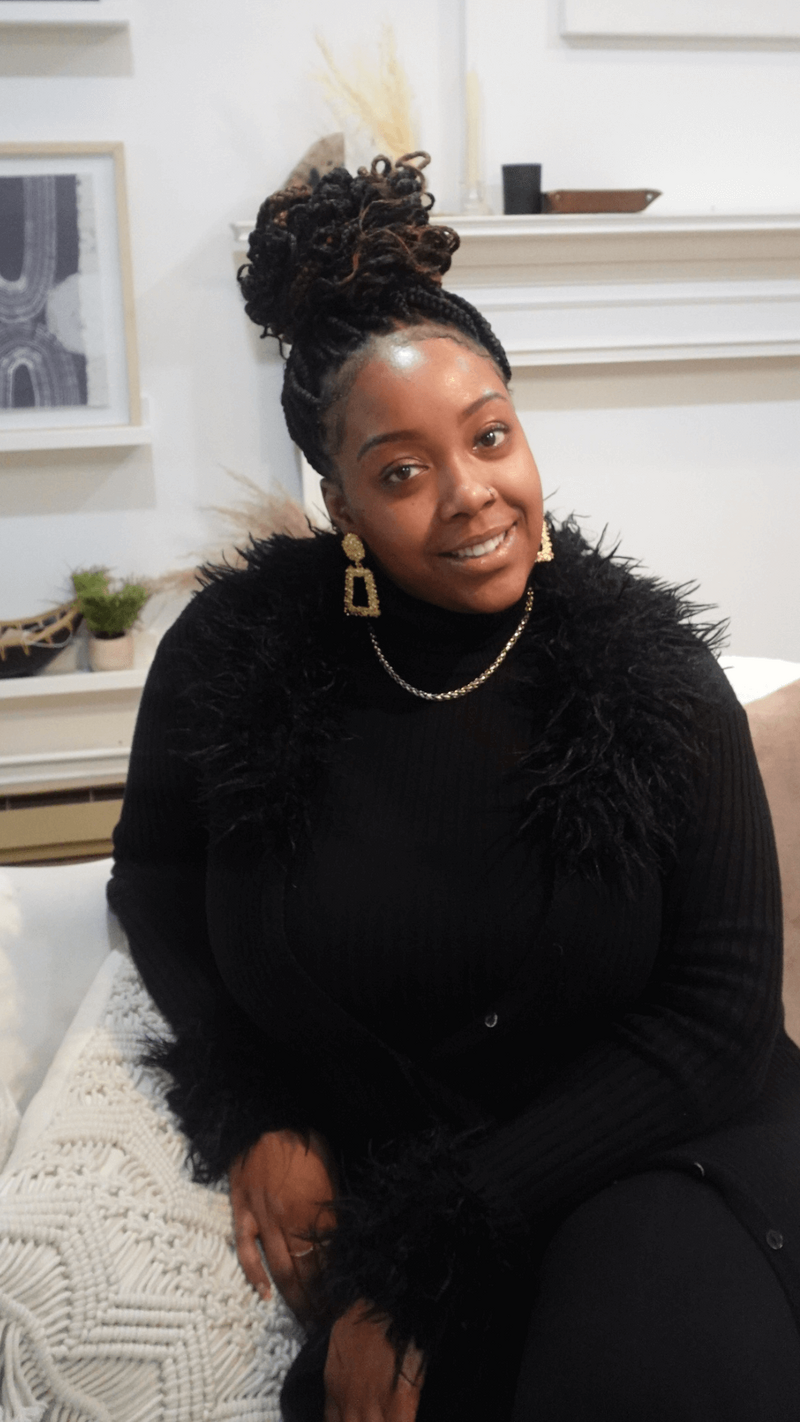 Black woman in black with gold earrings and hair in bun sitting on coach