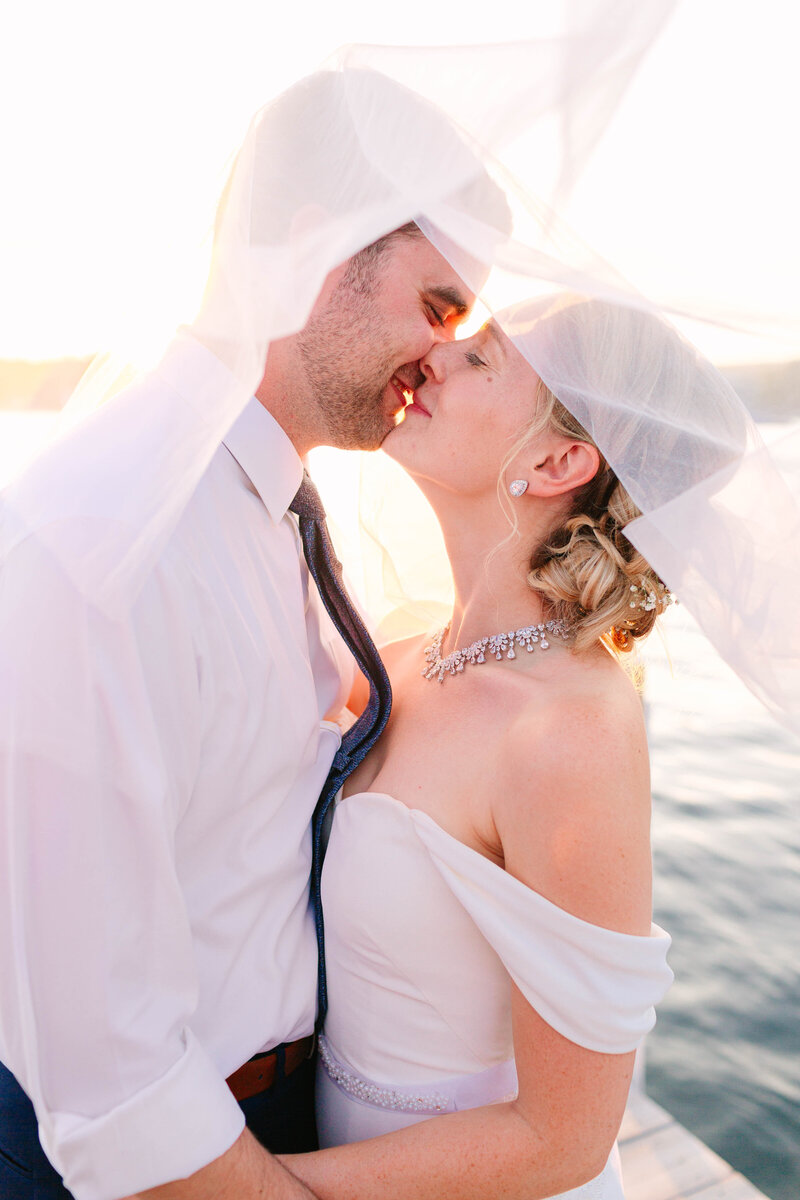 Bright and light wedding photo of a man and woman hugging outside in a suit and wedding dress with trees in the background