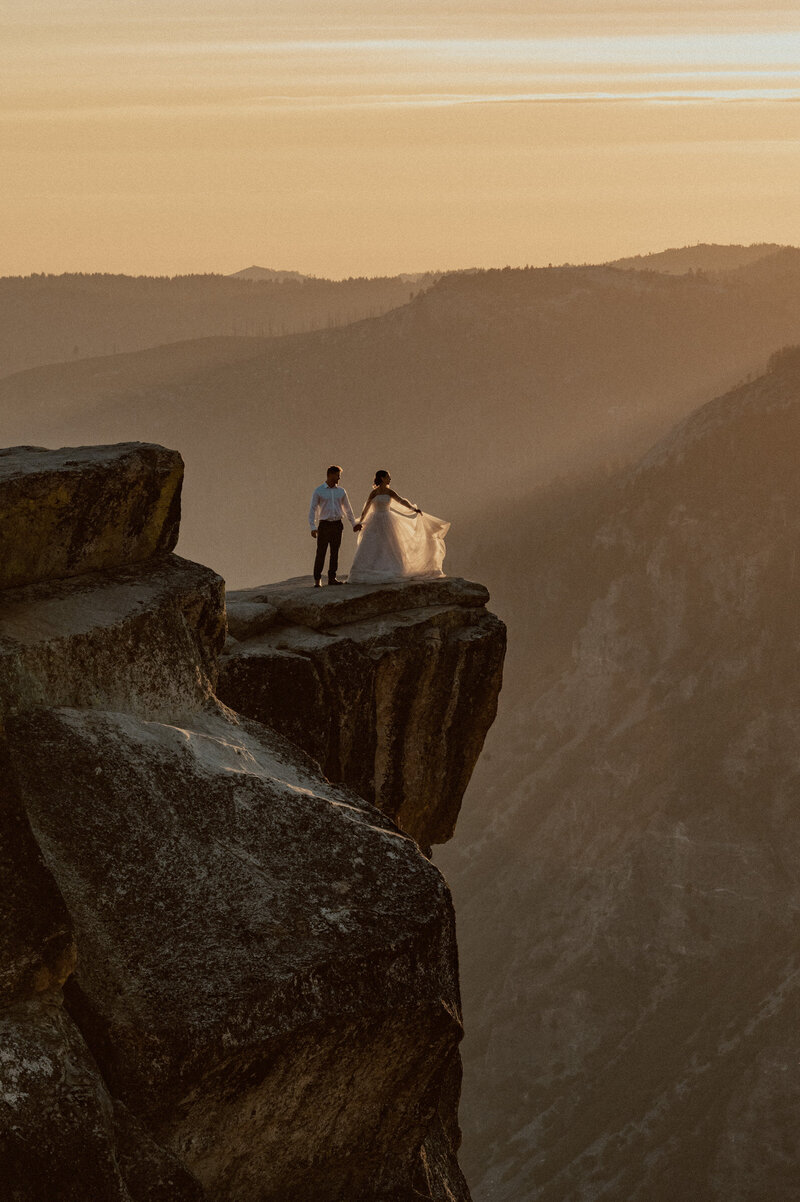 bride and groom on taft point with the sunset shining behind them, perfectly illuminating the layers of the brides dress