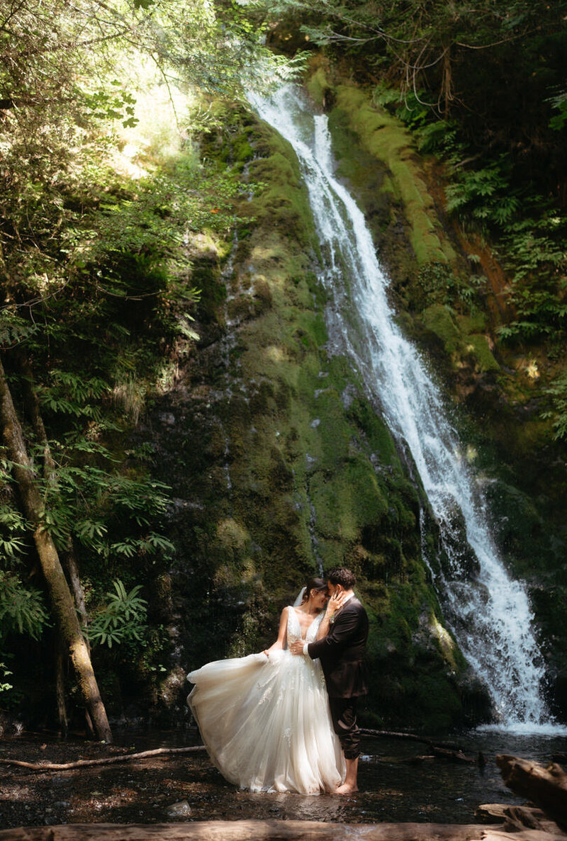 Elopement Photo Ideas | Standing underneath a waterfall, Bride tosses her dress as groom kisses her 