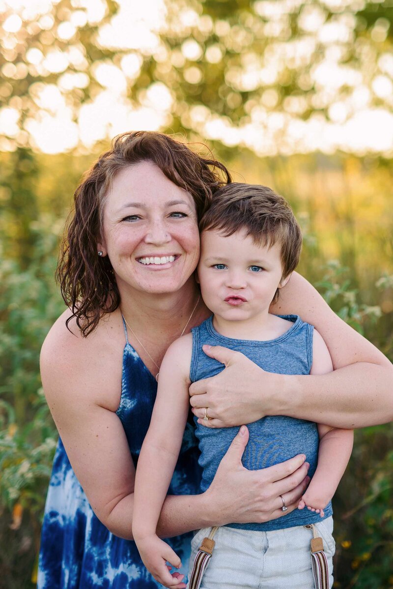 Jen Howell, Memphis professional newborn and family photographer, holds her son in a field at sunset.