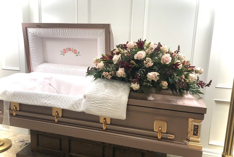 pink and burgundy funeral casket flowers laying on top of a casket