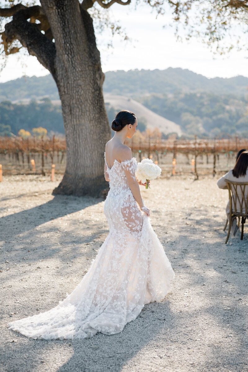 Bride walking down the aisle in a modern lace dress against a mountain and vineyard backdrp