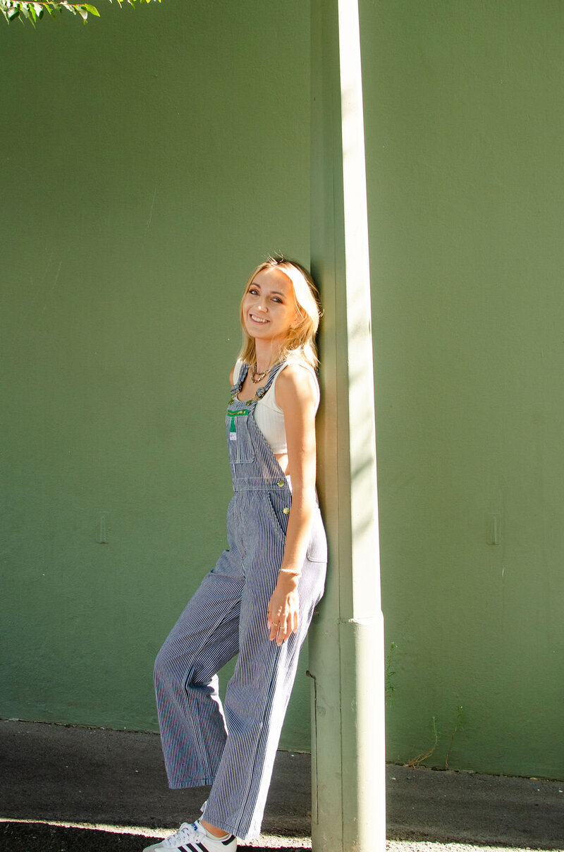 Jess in overalls standing in outside in green background
