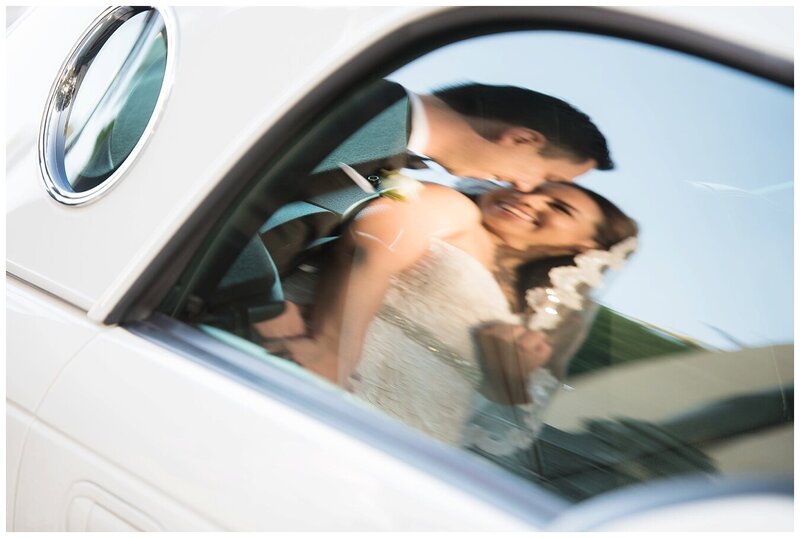 bride and groom reflection in car window, smiling while holding each other